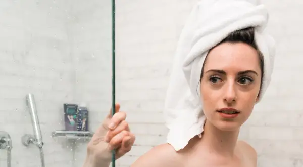 Ragazza con asciugamano in testa guarda preoccupata la doccia, pensando che la paraffina liquida fa male alla pelle.