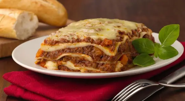 Pyszna, gorąca lasagne z mięsem i serem, idealna na obiad. Obok leżą świeże bagietki.