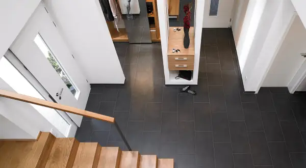 Moderner Flur nach Renovierung: Holzboden, dunkle Fliesen, Garderobe mit Spiegel und Blumen.