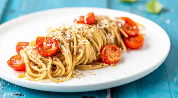 Spaghetti conditi con una cremosa salsa alle melanzane, guarniti con pomodorini confit e parmigiano grattugiato.