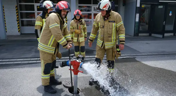 Jugendfeuerwehr übt den Umgang mit dem Hydranten. Wasser spritzt aus dem roten Standrohr, während die jungen Brandschützer in voller Montur zuschauen.