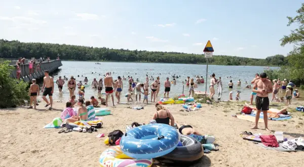 Tłum ludzi odpoczywa nad jeziorem w Wielkopolsce. Kąpielisko tętni życiem, w wodzie i na plaży widać wielu kąpiących się i plażowiczów.
