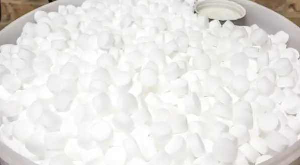 Un grand seau rempli de pastilles blanches de sel régénérant, prêtes à purifier l'eau.