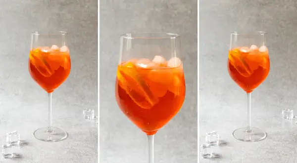 Trzy identyczne kieliszki z pomarańczowym drinkiem Aperol Spritz, lodem i plasterkami pomarańczy na szarym tle.