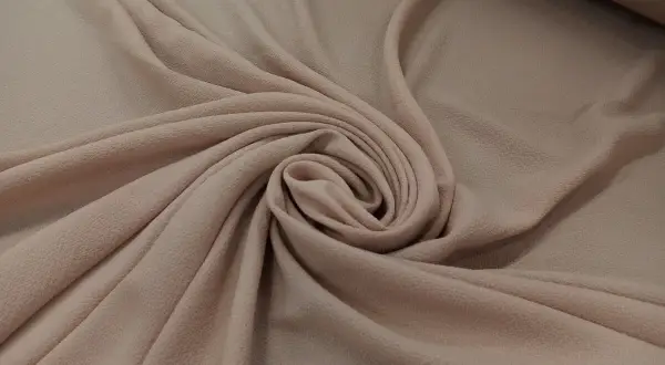 Delikatna, beżowa żorżeta układa się w miękkie fałdy, tworząc elegancką spiralę.