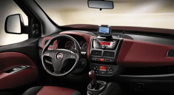 Interni Fiat Doblò con cruscotto rosso bordeaux, volante multifunzione, navigatore e radio.