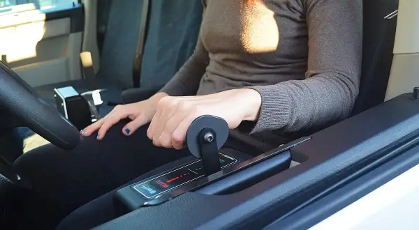 Mano che aziona la leva di un allestimento auto per disabili, con indicazioni "brake" e frecce.