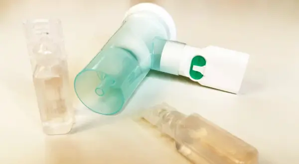 Nebulizator z zielonym przyciskiem i ampułkami, jedna z nich zawiera roztwór NaCl 0,9%.