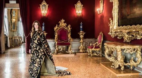 Donna con abito prezioso in una sala dorata, un'elegante tessitura Bevilacqua per una visita regale.