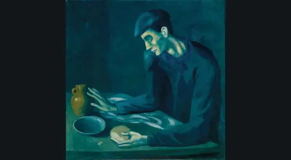 A man in a cap, characteristic of Picasso's Blue Period, sits at a table with a jug and bread, his face illuminated by a somber, blue light.