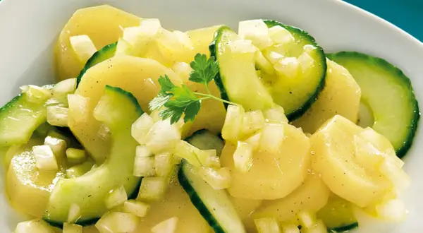 Ein appetitlicher Kartoffelsalat mit Gurken, verfeinert mit Zwiebeln und Petersilie.
