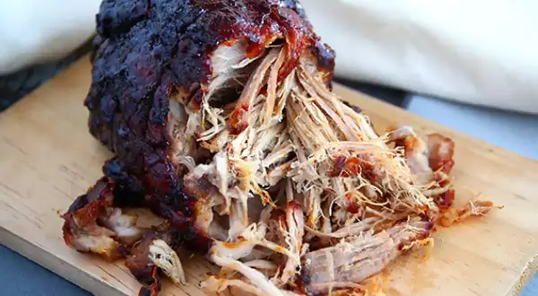Saftig pulled pork 12 timmar, perfekt tillagad och redo att serveras på en träskärbräda.