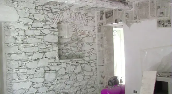 Interno con muro in pietra e intonaco grezzo, travi a vista e un compressore rosa.