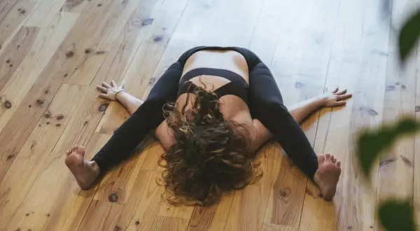 Pratique d'Ashtanga yoga : une femme en posture d'ouverture des hanches sur un parquet en bois.