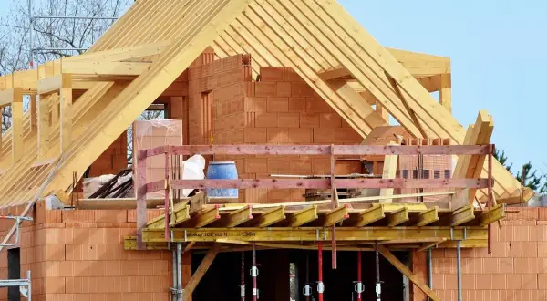 Budowa domu z cegły, widoczna drewniana konstrukcja dachu i balkon. Dopuszczalny błąd wymiarów budynku jest tu nieistotny, liczy się postęp prac.
