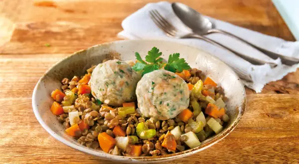 Zwei Semmelknödel auf Linsengemüse mit Karotten und Sellerie, garniert mit Petersilie.