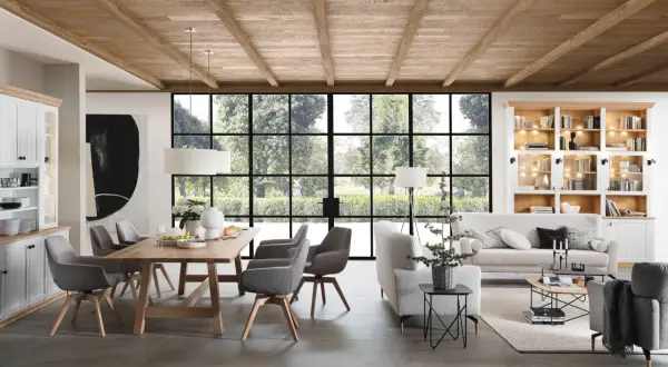 Rustikaler Holztisch mit grauen Stühlen, eine gemütliche Sofalandschaft und ein Bücherregal – perfekte esstisch inspo für ein helles Wohn-Esszimmer mit Blick ins Grüne.
