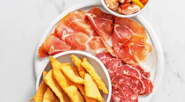 En tallrik med italienska delikatesser: tunt skivad prosciutto, salami och krispiga gnocco fritto. En skål med marinerade grönsaker.