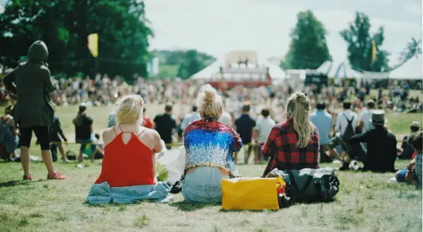 Festivalgäster sitter på gräset med en packlista i åtanke. En gul väska och en stor bag ligger redo för äventyr.