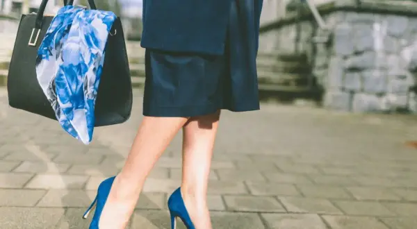 Elegancka kobieta w butach w kolorze szafirowym i granatowej spódnicy, niosąca torebkę z kwiecistym szalem.
