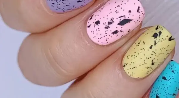 Delikatne, **milky nails** w pastelowych kolorach: fioletowym, różowym, żółtym i turkusowym, ozdobione czarnymi plamkami imitującymi skorupki jajek.