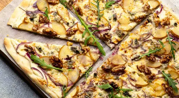 Ein köstlicher flammkuchen vegetarisch mit Birnenspalten, roten Zwiebeln, Walnüssen und Rucola.