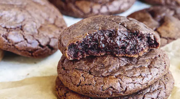 En hög med kladdkake cookies, en är uppäten och visar den sega, chokladiga insidan. Perfekt för fikat!