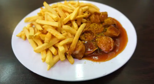 Eine Portion knuspriger Pommes Frites neben einer Currywurst in würziger Sauce, ein Klassiker aus Berlin.