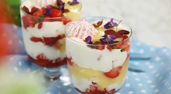 Två glas med Eton Mess, lager av vispad grädde, jordgubbar och maräng, toppade med blommor.