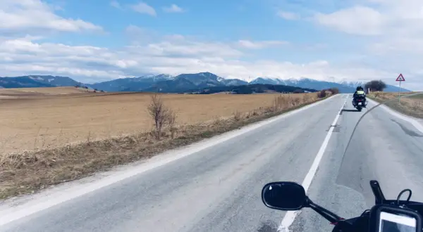 Motocykliści jadący drogą w kierunku ośnieżonych gór Tatr.