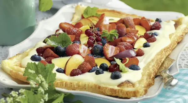 En långpanna med tårtbotten täckt av kräm och färska bär som jordgubbar, blåbär och hallon.