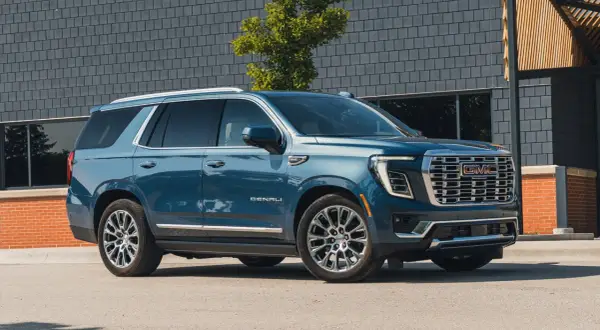 Niebieski GMC Yukon XL Denali lśni na tle nowoczesnej architektury.