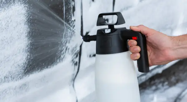 Mano che spruzza schiuma per lavare auto a casa con un'idropulitrice.