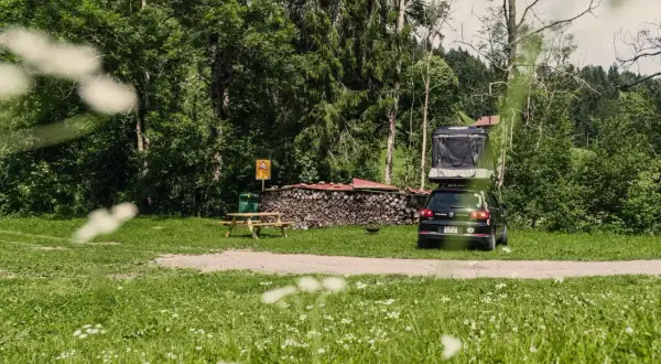 Campingplatz mit Dachzeltauto, Holzstapel und Picknicktisch. Ein idyllischer Ort für Basel Geheimtipps abseits des Trubels.