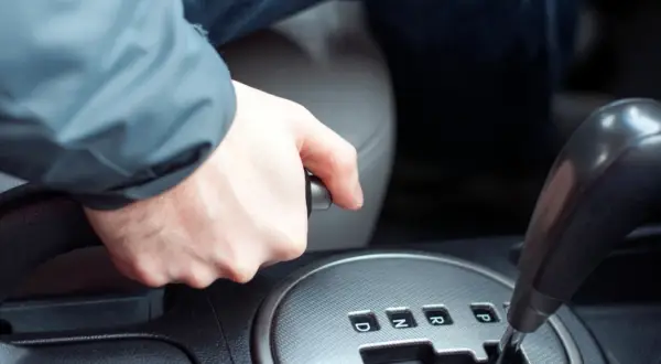 Main d'un conducteur actionnant le frein à main dans une voiture, prêt à démarrer.
