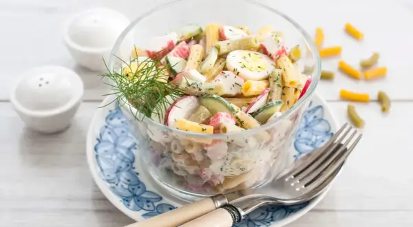 Salade de pâtes au surimi, œufs durs, concombre et radis, garnie d'aneth. Un délice frais et coloré.