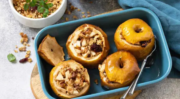 Mele cotte ripiene di frutta secca e granola, servite in una teglia blu.