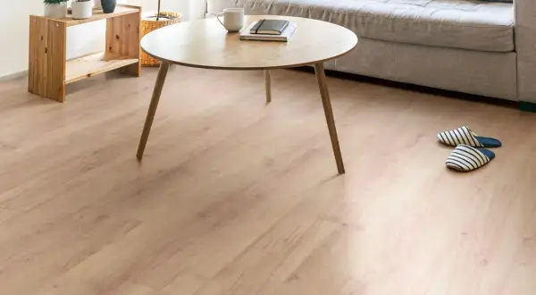 Un salón acogedor con un suelo laminado de madera clara, un sofá gris, mesa de centro de madera y plantas.