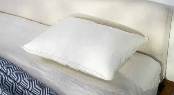 A plush white pillow rests on a neatly made bed, perfect for a comfortable night's sleep, especially for those who prefer to sleep on their stomach.