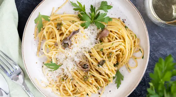 Spaghetti mit Sardellen, Kapern und Parmesan, garniert mit Petersilie. Ein köstliches Gericht, das Meer und Land vereint.