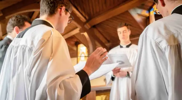 Jeunes hommes en surplis, se préparant pour un baptême protestant. L'un lit un texte, l'autre écoute attentivement.