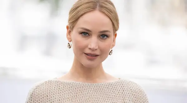 Jennifer Lawrence, gwiazda wielu filmów, w beżowym swetrze i złotych kolczykach.
