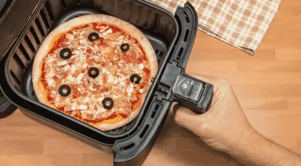 Une pizza garnie d'olives noires et de fromage est prête à être cuite dans un airfryer.