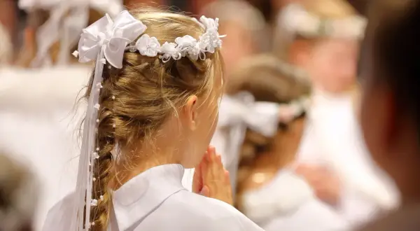 Dziewczynka w białej sukience i wianku modli się. To piękny widok, co na komunie.