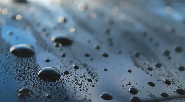 Krople wody na ciemnej powierzchni samochodu, świadczące o działaniu powłoki hydrofobowej.