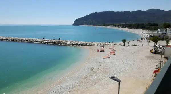 Mattinata serena sulla spiaggia di piana, con il mare azzurro che lambisce la costa ghiaiosa e il molo di sassi.