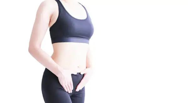 Femme en tenue de sport, mains sur le bas-ventre. Une solution pour la fuite urinaire pendant le sport.