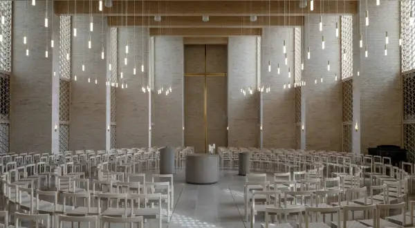Innenraum einer modernen Kirche mit Reihen von Holzbänken, einem goldenen Kreuz und vielen hängenden Lichtern.
