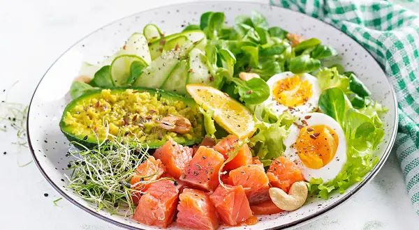 Un'idea per cosa mangiare a pranzo: un piatto colorato con salmone a cubetti, avocado, uova sode, cetrioli e germogli.