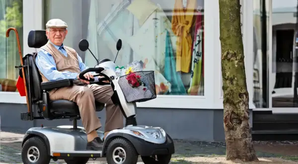 Älterer Herr im elektrischen Rollstuhl vor einem Schaufenster. Dank der Krankenkasse kann er mobil bleiben.